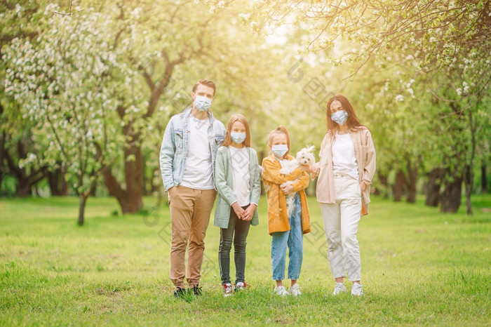 家庭面具在户外家庭穿保护医疗面具为防止病毒的公园可爱的家庭盛开的樱桃花园面具