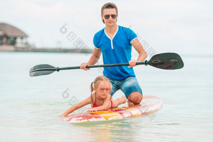 家庭爸爸和小女儿有有趣的站划在一起的海洋家庭爸爸和孩子们冲浪板在夏天假期