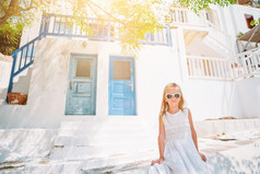 小可爱的女孩衣服在户外老街道米克诺斯孩子街典型的希腊传统的村与白色墙和色彩斑斓的门米克诺斯岛希腊小可爱的女孩衣服在户外老街道米克诺斯