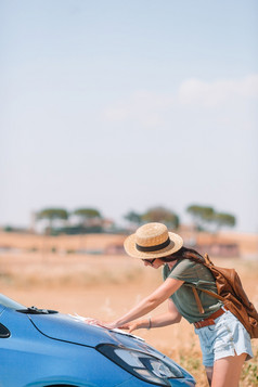 年轻的女人看为的正确的道路在旅行车旅游女孩托斯卡纳假期女人为新冒险看为的正确的道路的地图