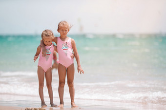 小女孩有有趣的热带海滩玩在一起可爱的小姐妹海滩在夏天假期小快乐有趣的女孩有很多有趣的热带海滩玩在一起阳光明媚的一天与雨的海