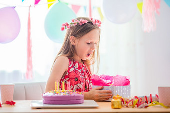 快乐小女孩拆包现在她的生日生日聚会，派对和祝愿概念高加索人女孩如痴如梦微笑和看生日彩虹蛋糕节日色彩斑斓的背景与气球生日聚会，派对和祝愿概念