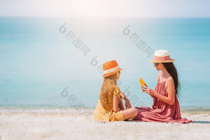 妈妈。应用太阳奶油女儿手太阳保护的海滩年轻的妈妈。应用太阳奶油女儿鼻子的海滩太阳保护