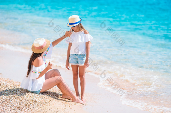 妈妈。应用太阳奶油她的小女儿太阳保护的海滩年轻的妈妈。应用太阳奶油女儿鼻子的海滩太阳保护