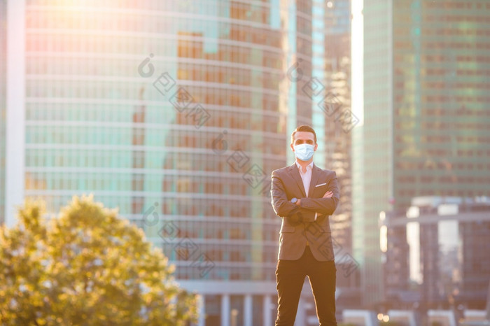 商人穿面具为防止病毒城市城市与摩天大楼建筑的背景商人看复制空间而站对玻璃摩天大楼