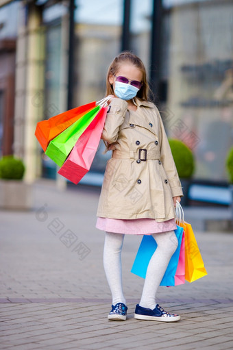 可爱的小女孩穿面具为防止病毒走与购物袋在户外欧洲城市肖像可爱的小女孩面具走与购物袋在户外欧洲城市