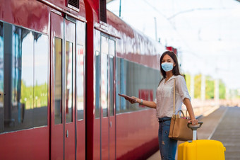 女人穿面具为防止病毒与行李的平台旅行航空快线保护对冠状病毒和抓手年轻的旅游女人与行李的平台等待为火车