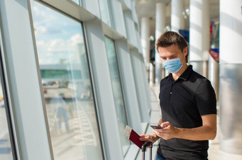 男人。穿面具为防止病毒国际机场休息室等待为飞行飞机保护对冠状病毒和抓手年轻的男人。机场休息室等待为飞行飞机