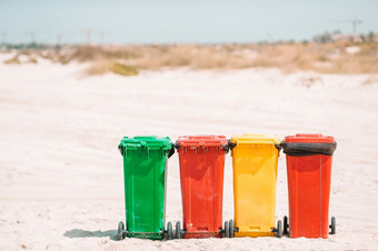 明亮的塑料容器为垃圾排序的海滩红色的黄色的蓝色的和绿色容器为玻璃塑料废物和纸的沙子海滩的海边生态和回收概念四个塑料容器为垃圾排序的海滩