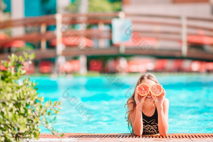 快乐小女孩涵盖了眼睛与红色的橙子摆姿势背景游泳池小女孩覆盖眼睛与橙色半附近眼睛背景游泳池