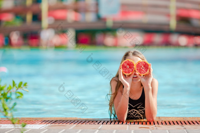 小女孩涵盖了眼睛与橙子摆姿势孤立的在游泳池小女孩覆盖眼睛与橙色半附近眼睛背景游泳池