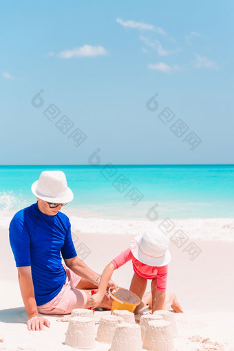 父亲与他的孩子玩与沙子热带海滩父亲和孩子使沙子城堡热带海滩家庭玩与海滩玩具