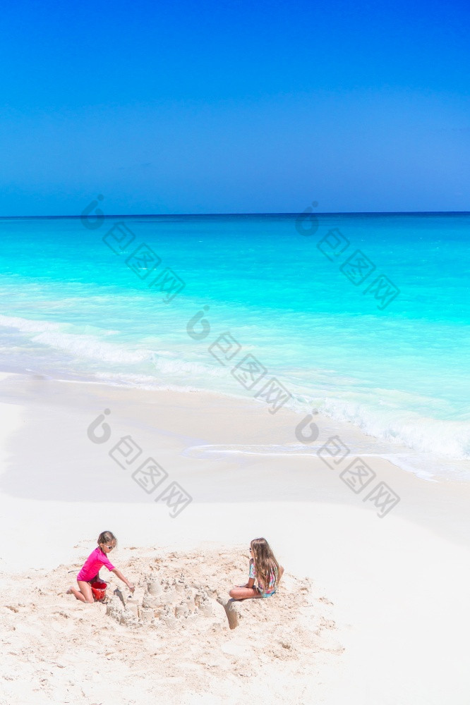小女孩有有趣的热带海滩玩在一起和使沙塔两个小快乐女孩有很多有趣的热带海滩玩在一起