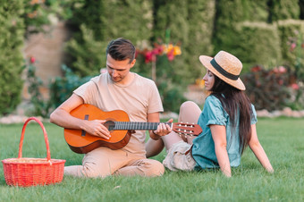 快乐家庭放松夏天野餐男人。持有的吉他和女人与白色小狗年轻的夫妇旅游享受夏天假期
