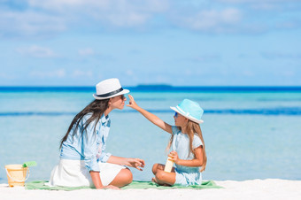 小孩子应用太阳奶油妈妈鼻子的海滩的概念保护从紫外线辐射年轻的妈妈。应用太阳奶油女儿鼻子的海滩