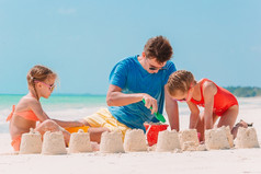 父亲和两个女孩玩与沙子热带海滩父亲和孩子们使沙子城堡热带海滩家庭玩与海滩玩具