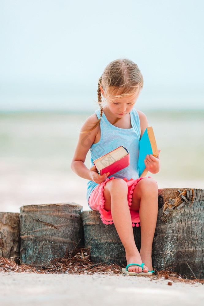 小女孩阅读书的海滩小的女孩阅读书在热带海图片
