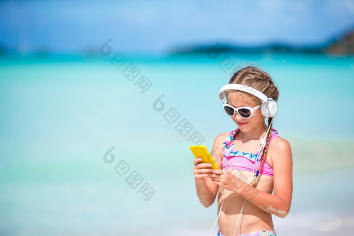 小女孩听的音乐耳机的海滩小可爱的女孩听音乐背景海