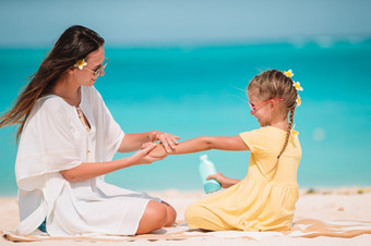 快乐女人应用太阳奶油女儿手太阳保护的海滩年轻的妈妈。应用太阳奶油女儿鼻子的海滩太阳保护