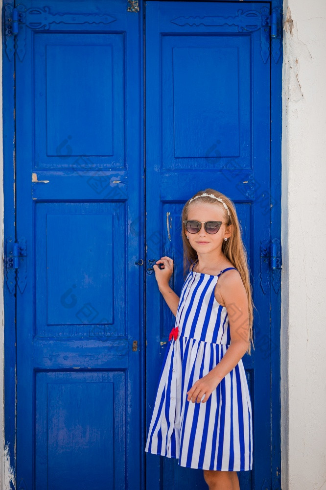 可爱的小女孩衣服老街典型的希腊传统的村与白色墙和蓝色的门可爱的小女孩老街典型的希腊传统的村