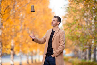 秋天概念快乐男人。喝咖啡秋天公园下秋天树叶年轻的男人。喝咖啡与电话秋天公园在户外