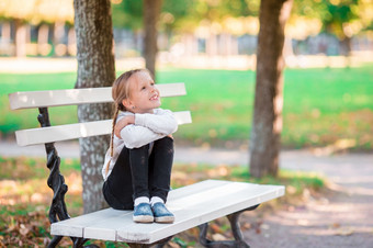 可爱的小女孩坐着失去了认为美丽的温暖的春天一天在户外小女孩的板凳上的公园可爱的小女孩美丽的秋天一天在户外