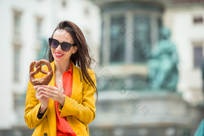 美丽的年轻的女人持有椒盐卷饼和放松公园欧洲美丽的年轻的女人持有椒盐卷饼和放松公园