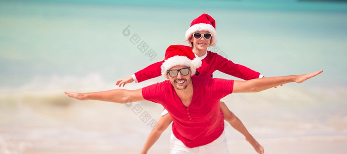 小可爱的女孩和年轻的父亲圣诞老人他在海滩圣诞节假期父亲和女儿圣诞老人他有有趣的热带海滩