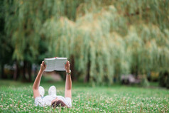 年轻的美丽的女孩阅读书的公园在户外放松年轻的女人阅读书