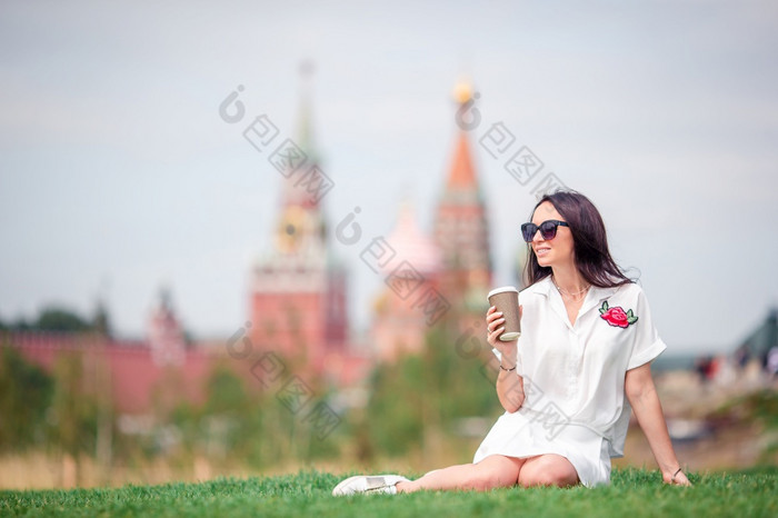快乐年轻的城市女人喝咖啡在户外大城市放松的草肖像微笑女孩与饮料手快乐年轻的城市女人喝咖啡欧洲城市