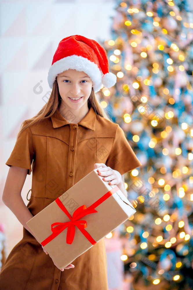 美丽的小女孩与礼物盒子附近的圣诞节树快乐圣诞节和快乐假期回来视图孩子持有礼物盒子附近的圣诞节树在室内