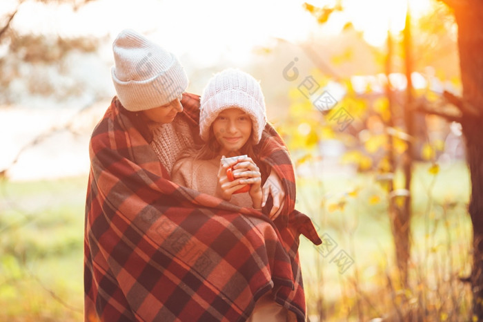 快乐妈妈。和小女孩与杯子秋天一天包装毯子美丽的家庭秋天温暖的一天在一起