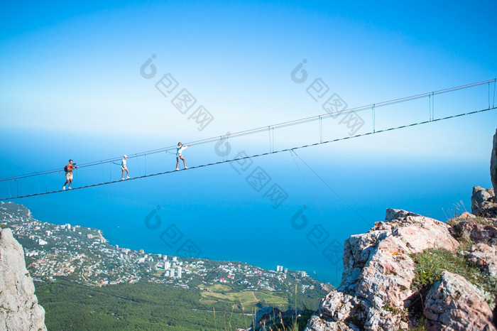 家庭勇敢的父亲和孩子们悬架桥对的背景的海和山家庭穿越的鸿沟的绳子桥黑色的海背景克里米亚俄罗斯