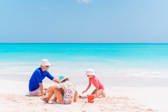 父亲和两个女孩玩与沙子热带海滩家庭玩与海滩玩具父亲和孩子们使沙子城堡热带海滩家庭玩与海滩玩具