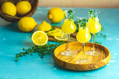 Limoncello与百里香三个格拉巴酒葡萄酒杯木托盘新鲜的柠檬篮子光混凝土表格艺术仍然生活光背景