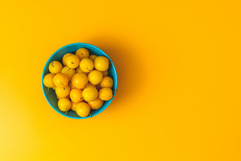 有创意的夏天模式使新鲜的黄色的樱桃李子蓝色的碗柔和的黄色的背景水果最小的概念平躺