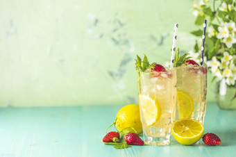 两个眼镜冷冰冷的让人耳目一新喝与柠檬和草莓服务与酒吧工具绿色木表格与白色盛开的花新鲜的鸡尾酒饮料与冰水果和草装饰