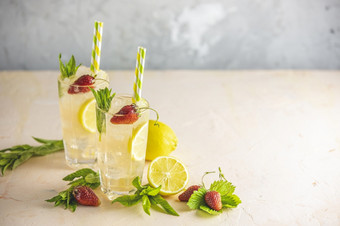 两个眼镜冷冰冷的让人耳目一新喝与柠檬和草莓服务与酒吧工具光粉红色的表格新鲜的鸡尾酒饮料与冰水果和草装饰