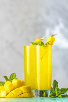 让人耳目一新夏天鸡尾酒使芒果冷喝喝与冰蓝色的灰色的背景新鲜的夏天冰冷芒果鸡尾酒汁与薄荷和芒果水果