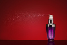 喷涂香水从雾化器紫色的玻璃香水瓶与细破裂蒸汽可见对红色的工作室背景与渐晕