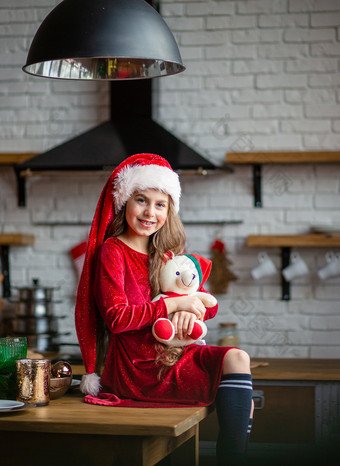 快乐圣诞节可爱的小女孩圣诞老人他持有泰迪熊坐着的厨房等待为的假期时间奇迹和实现欲望快乐圣诞节可爱的小女孩圣诞老人他持有泰迪熊坐着的厨房等待为的假期