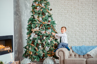 可爱的男孩装修的圣诞节树与圣诞节球礼物下的圣诞节树快乐圣诞节可爱的男孩装修的圣诞节树与圣诞节球礼物下的圣诞节树
