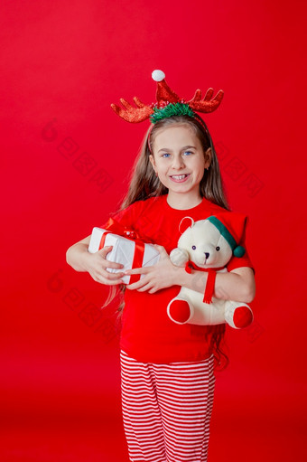 肖像有趣的快乐的女孩与绷带角她的头拥抱泰迪熊圣诞节睡衣孤立的明亮的红色的背景的孩子点手的地方为文本肖像有趣的快乐的女孩与绷带角她的头拥抱泰迪熊圣诞节睡衣孤立的明亮的红色的背景