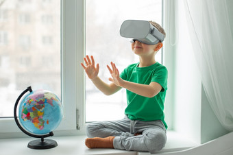 男孩与虚拟现实耳机坐着首页的表格在室内的孩子探讨了的世界虚拟现实通过视频和游戏技术的未来男孩与虚拟现实耳机坐着首页的表格在室内的孩子探讨了的世界虚拟现实通过视频和游戏