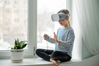 孩子与虚拟现实耳机坐着的表格在室内首页女孩探索的世界虚拟现实通过视频和游戏技术的未来孩子与虚拟现实耳机坐着的表格在室内首页女孩探索的世界虚拟现实通过视频和游戏