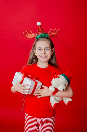 肖像有趣的快乐的女孩与绷带角她的头拥抱泰迪熊圣诞节睡衣孤立的明亮的红色的背景的孩子点手的地方为文本肖像有趣的快乐的女孩与绷带角她的头拥抱泰迪熊圣诞节睡衣孤立的明亮的红色的背景