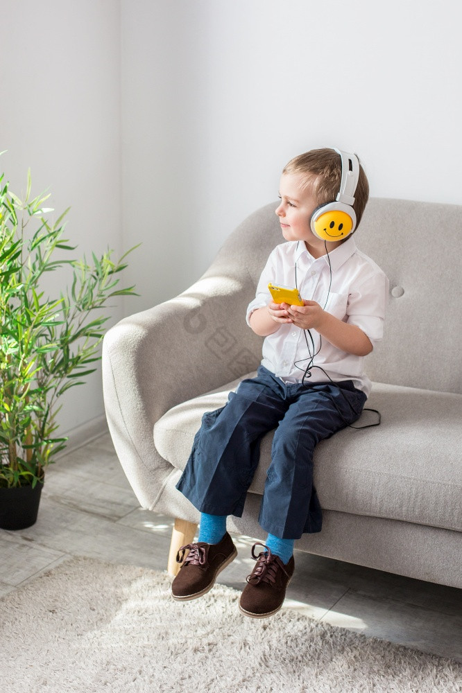 男孩听音乐与耳机坐着的沙发上男孩听音乐图片