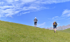 徒步旅行者攀爬长满草的山高山山下蓝色的天空