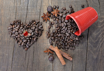 心形状的珠宝豆子咖啡形成心下一个泄漏红色的杯完整的豆子木背景心形状的珠宝豆子咖啡形成心下一个泄漏红色的杯完整的豆子木背景