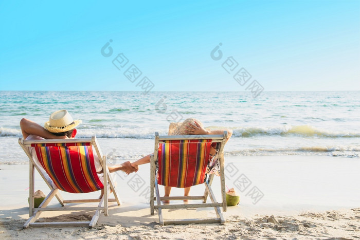 放松夫妇躺下来海滩椅子与海波背景男人。和女人有假期海自然概念放松夫妇躺下来海滩椅子与海波背景